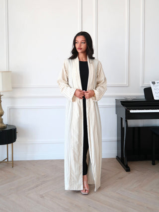Minimalist beige striped abaya with open front worn over black dress in elegant neutral interior
