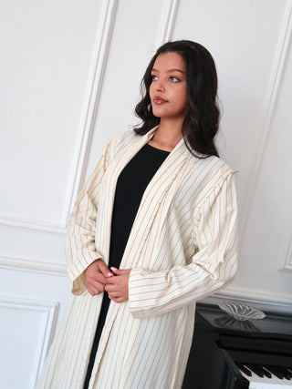 Close up of cream pinstripe abaya with relaxed fit layered over black outfit, soft natural light setting