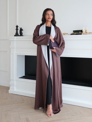 Reversible brown abaya in double sided silk with satin finish, worn open over black dress in minimal interior