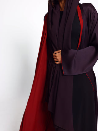 Person wearing a dark purple abaya with red accents on a white background
